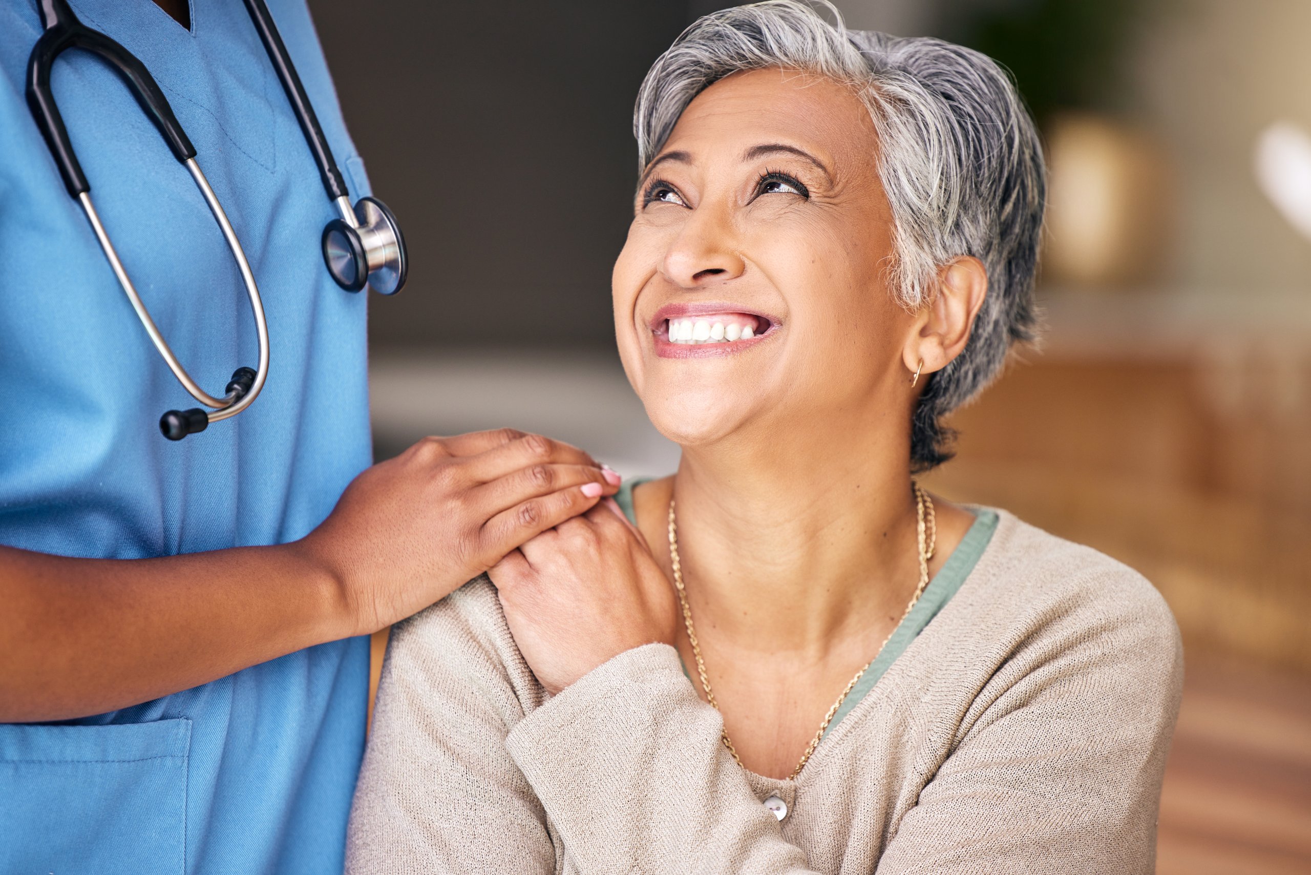 A healthcare worker touches a smiling older woman's shoulder.