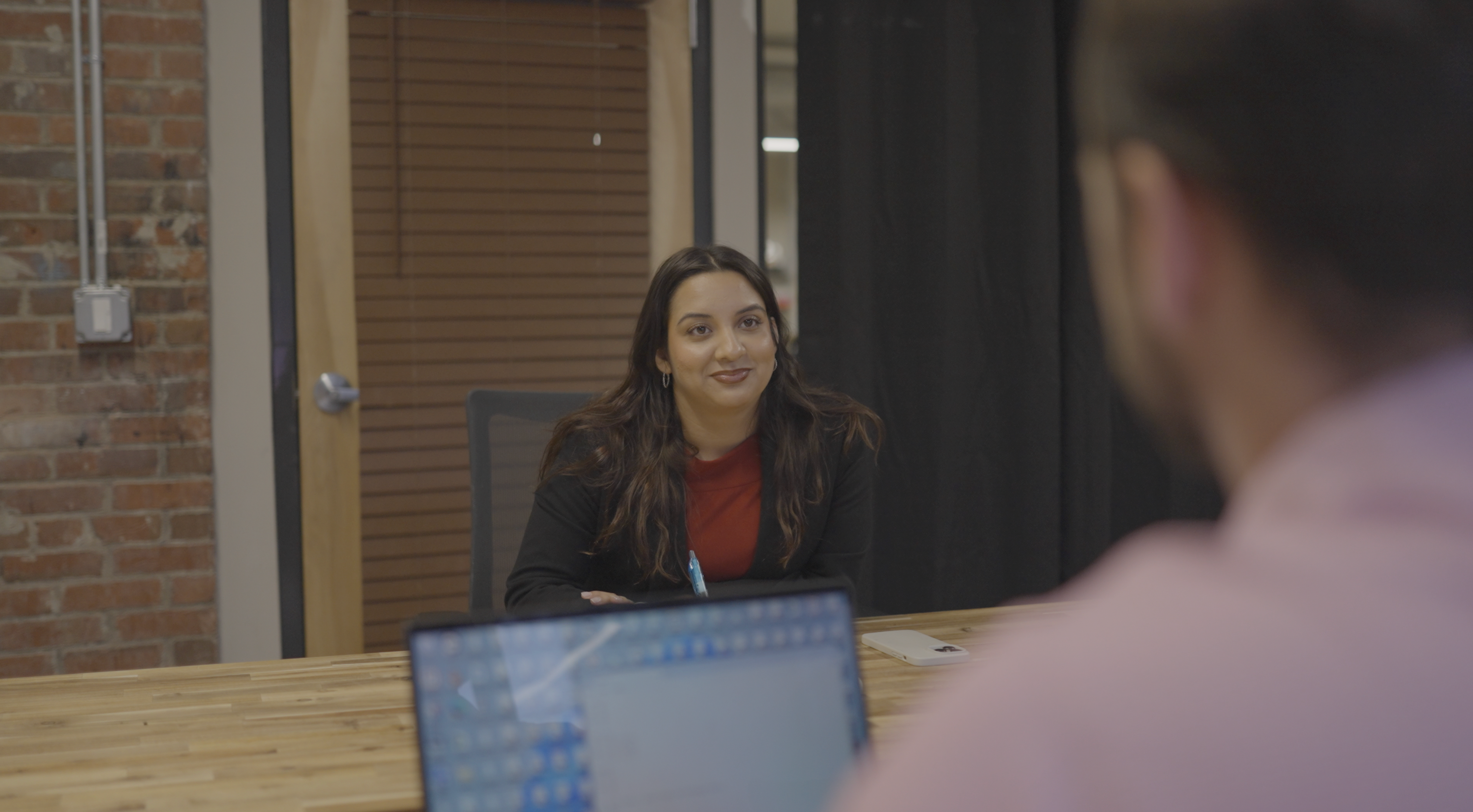 Monique Marin sits at a desk looking at a client across the table