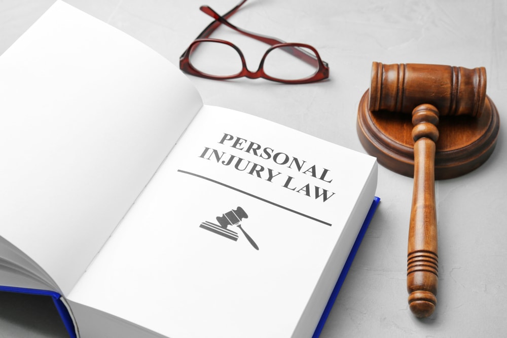 Closeup of the phrase "Personal Injury Law" printed in a book with a gavel and glasses in the background