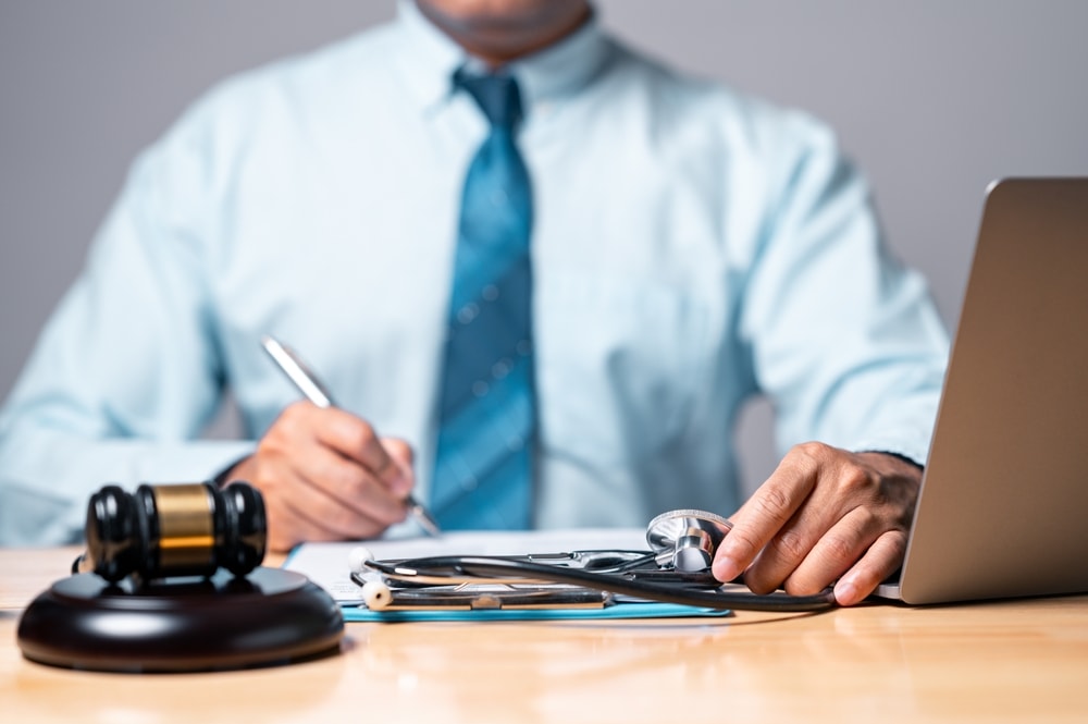 Personal injury lawyer sitting at a desk with a computer, gavel and stethoscope beside him