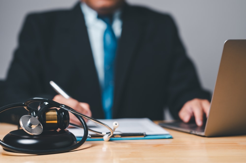 Personal injury lawyer sitting at a desk with a computer, gavel and stethoscope beside him